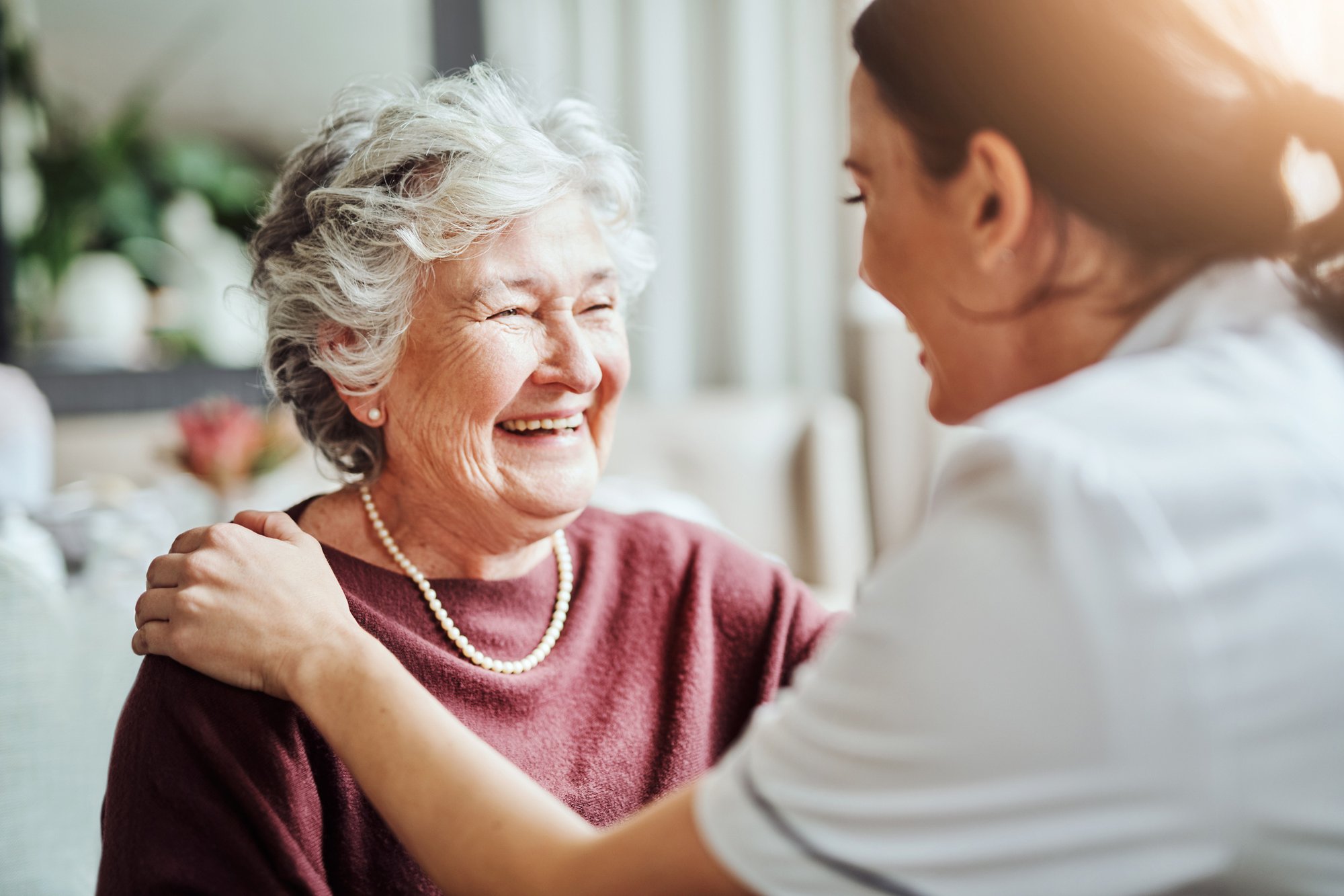 Elderly woman smiling while a caregiver puts her hand on her shoulder